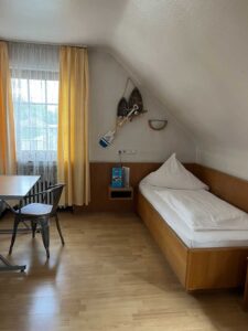 Standard-Einzelzimmer in der Aal-Kate Wuppertal mit Holzbett, Sitzgelegenheit am Fenster und maritimer Dekoration unter der Dachschräge.