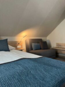 Detailaufnahme im Komfort-Doppelzimmer der Aal-Kate Wuppertal mit Doppelbett, Couch, Dachschräge und stimmungsvoller Beleuchtung.
