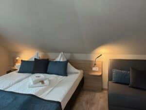 Komfort-Doppelzimmer in der Aal-Kate Wuppertal mit liebevoll gemachtem Doppelbett, frischen Handtüchern, Sofa und gemütlicher Beleuchtung unter der Dachschräge.