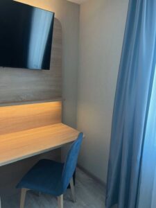 Schreibtisch mit Stuhl und Wandfernseher im Komfort-Doppelzimmer der Aal-Kate Wuppertal, ideal zum Arbeiten oder Entspannen am Fenster.