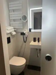 Modernes Badezimmer im Komfort-Einzelzimmer der Aal-Kate Wuppertal mit WC, Waschbecken, Spiegel mit Beleuchtung und Handtuchheizung.