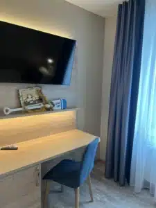 Arbeitsbereich im Komfort-Einzelzimmer der Aal-Kate Wuppertal mit Schreibtisch, Stuhl, großem Fernseher und Fenster mit Tageslicht.