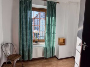 Durchgangszimmer im Apartment der Aal-Kate Wuppertal mit Stuhl, Fenster und Blick auf Fachwerkhaus – Verbindung zwischen Schlafzimmern und Bad.