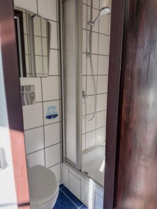 Modern gefliestes Badezimmer im Apartment der Aal-Kate Wuppertal mit Dusche, WC und Spiegel in neutralem Weiß-Blau-Design.