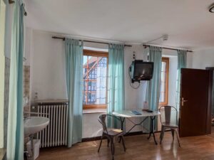 Aufenthaltsbereich im Apartment der Aal-Kate Wuppertal mit Tisch, Stühlen, Waschbecken, großem Fenster mit Blick und einem Wandfernseher.