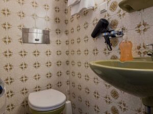 WC und Waschbecken im Standard-Einzelzimmer der Aal-Kate Wuppertal mit Retro-Fliesen, Wandfön und klassischer Ausstattung.