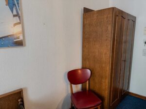 chrank und Stuhl im Standard-Einzelzimmer der Aal-Kate Wuppertal mit maritimer Wanddekoration und klassischer Holzeinrichtung.