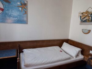 Standard-Einzelzimmer in der Aal-Kate Wuppertal mit schlichtem Einzelbett, maritimer Wanddekoration und funktionaler Ausstattung.