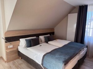 Geräumiges Komfort-Doppelzimmer in der Aal-Kate Wuppertal mit Doppelbett unter der Dachschräge, großem Fenster und modernen Holzelementen.