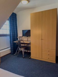 Economy-Einzelzimmer in der Aal-Kate Wuppertal mit Schreibtisch, Stuhl, Fernseher und Kleiderschrank in schlichtem Design.