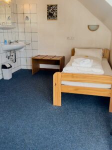 Economy-Einzelzimmer in der Aal-Kate Wuppertal mit Einzelbett, Waschbecken, Spiegel, Fliesenwand und schlichter Möblierung unter der Dachschräge.